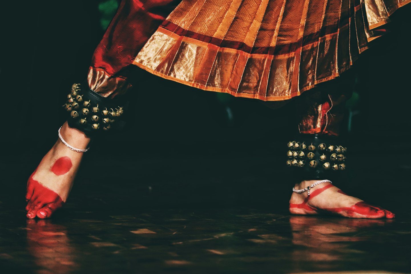 Dancer wearing silver ghungroo bells performs on stage.