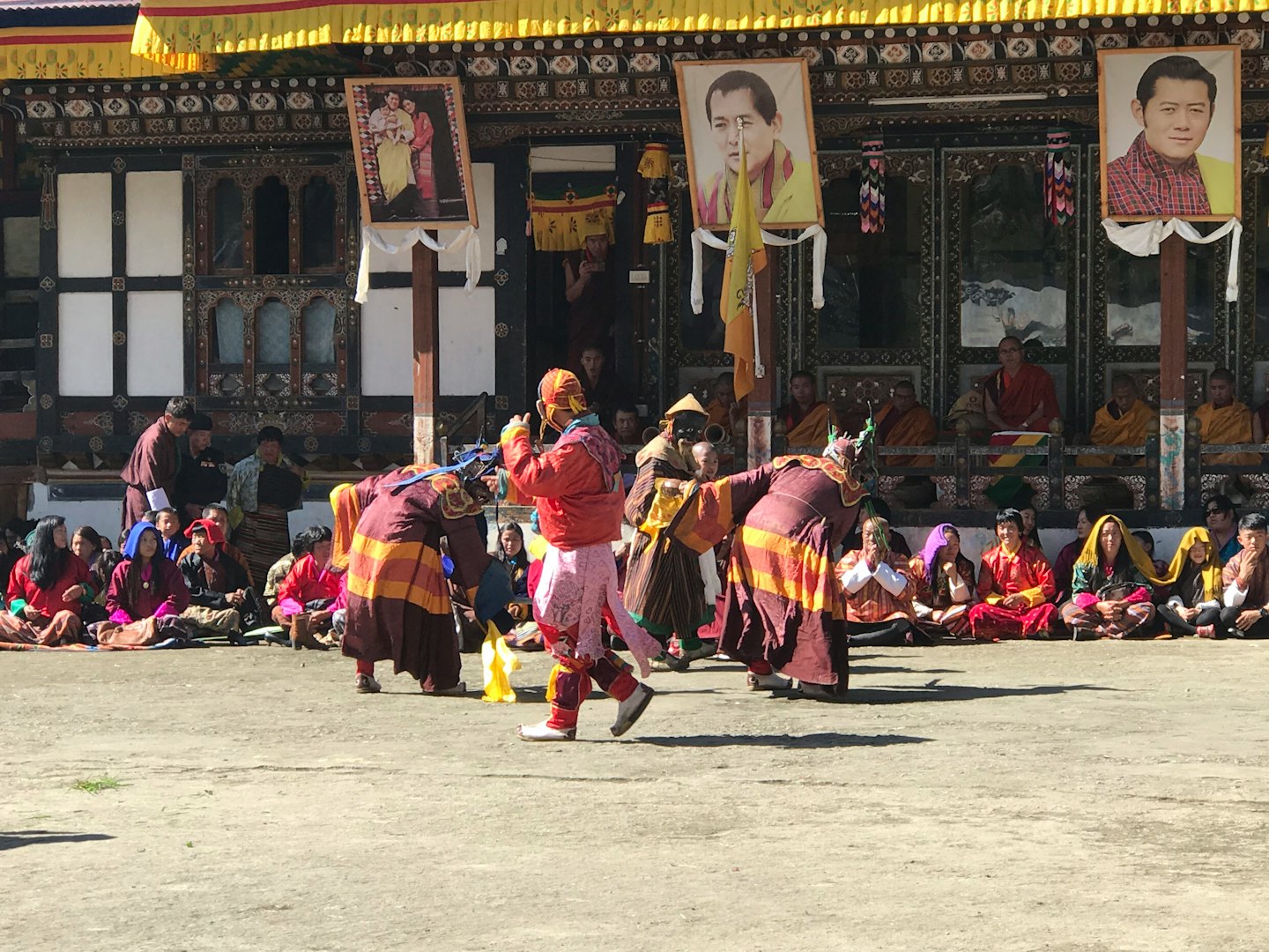 People in colorful costumes dance before a decorated building.