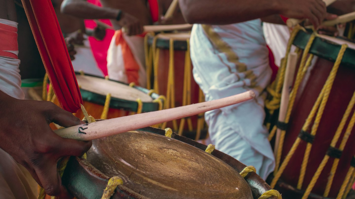Musicians playing traditional drums with wooden sticks.