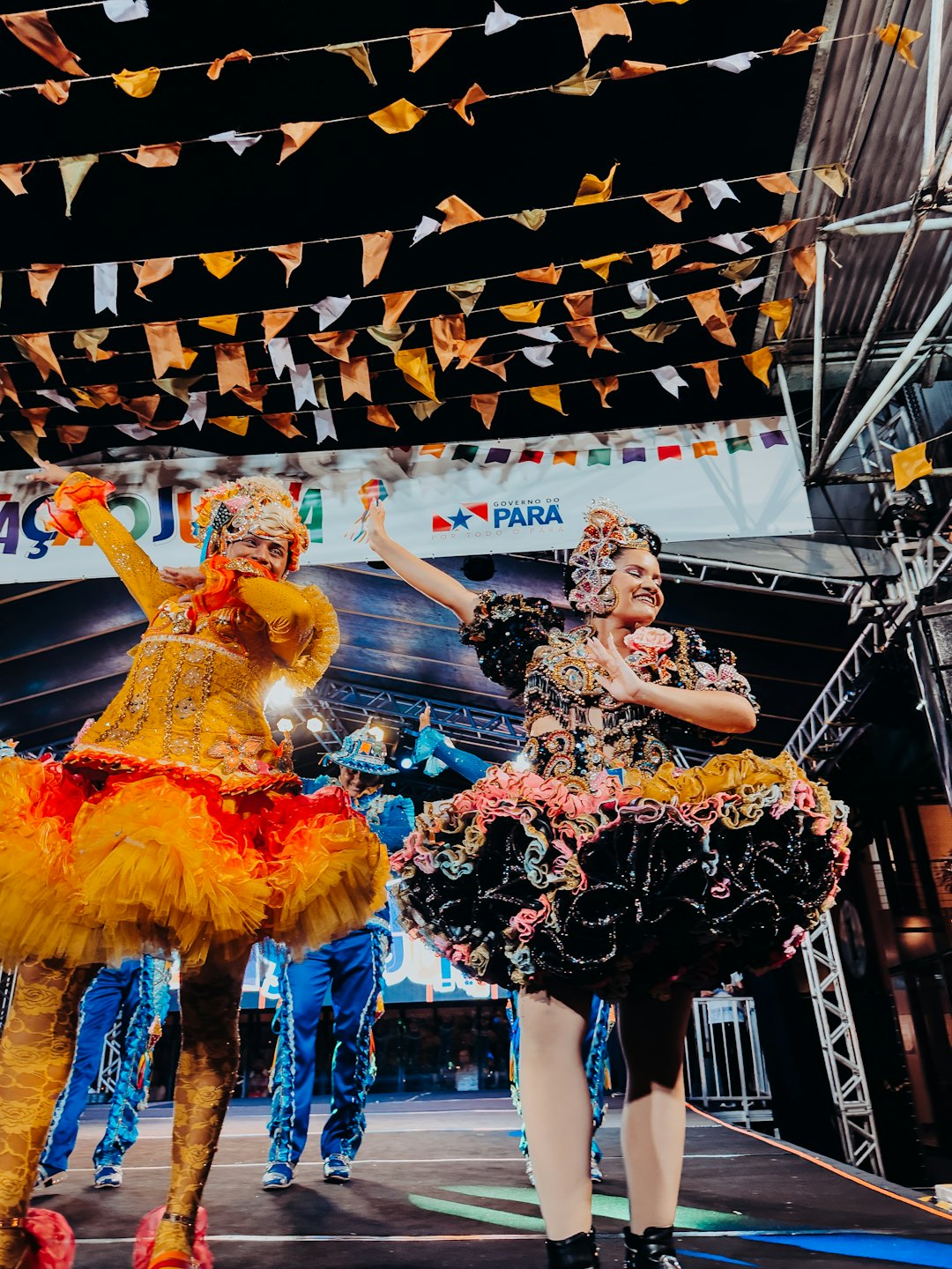 Two women in colorful traditional costumes dance on an outdoor stage.