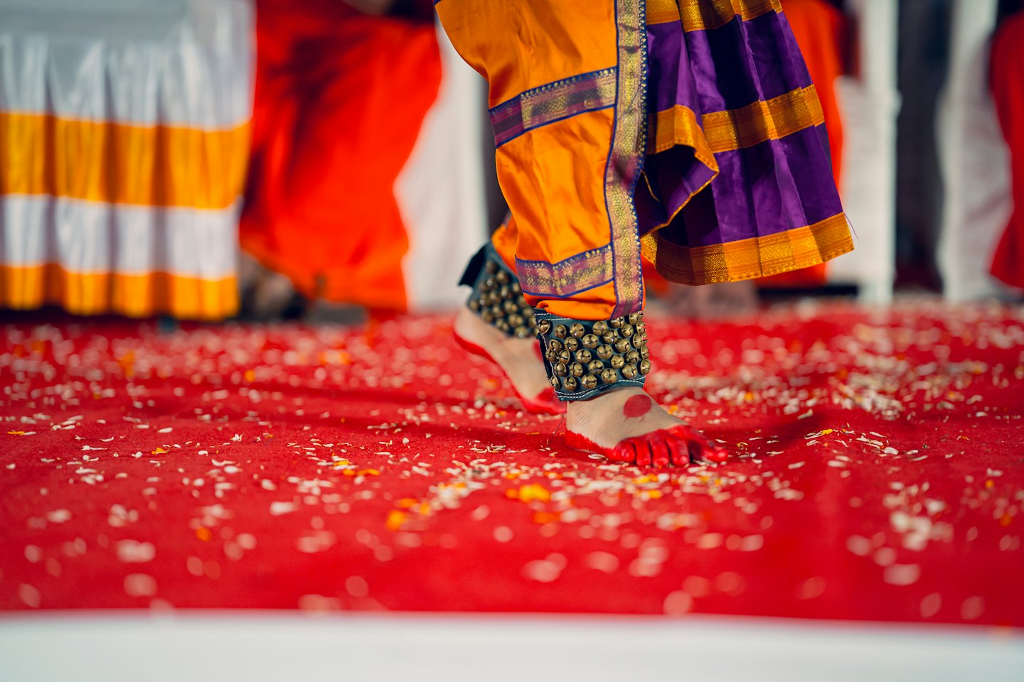 Dancer wearing ankle bells performs on a carpet covered in petals.